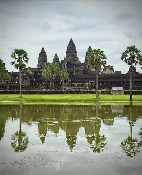       Angkor Wat main towers reflected in a moat with scaffolding on the ancient facade.
  
