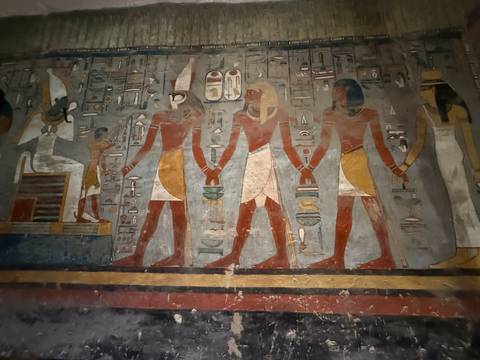       Ancient Egyptian wall painting depicting deities holding hands inside tomb.
  