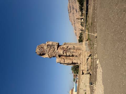       Colossus of Memnon statue standing solitary against clear blue sky in Luxor.
  