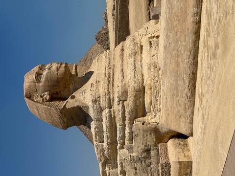       Iconic Great Sphinx of Giza with pyramid backdrop under clear blue sky.
  