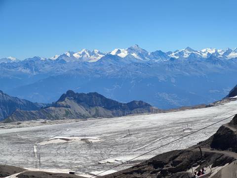       High alpine panorama of glacier fields with distant snow-covered peaks in the Alps.
  