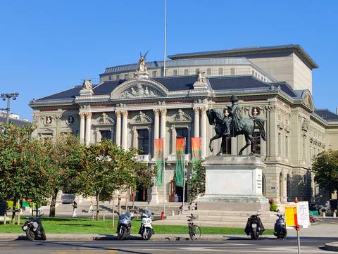       Grand neoclassical theatre with equestrian statue and columned façade in Swiss city.
  