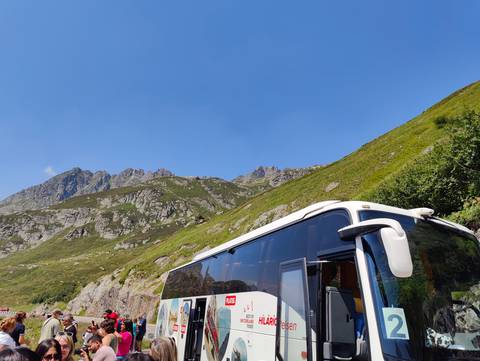       Tour coach parked on a winding alpine road with rocky mountainside in background.
  
