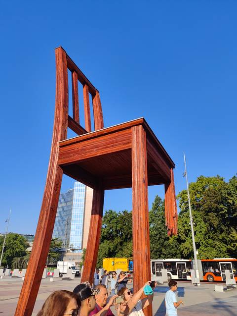       Large wooden 'Broken Chair' sculpture standing in urban square on sunny day.
  