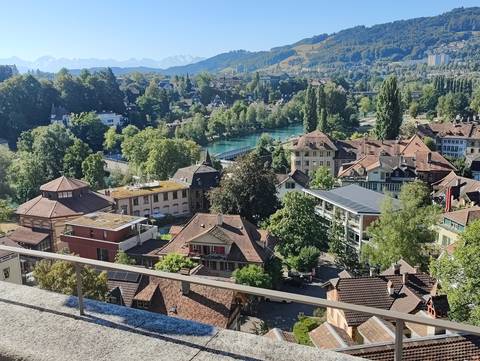       Panoramic view over Bern rooftops and the turquoise Aare River with mountains beyond.
  