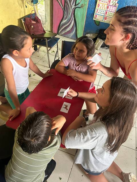       Volunteer shows animal flashcards to small children gathered around a red table.
  