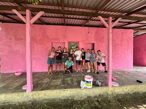       Group of volunteers in paint-splattered clothes pose proudly outside a newly pink-painted building.
  