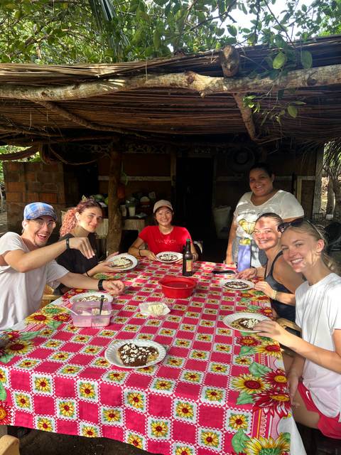      Travellers share a home-cooked meal at a colourful outdoor table with a local host.
  