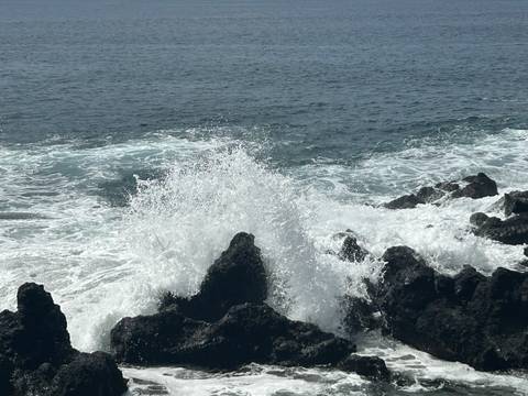       Powerful ocean waves crash dramatically against jagged black volcanic rocks sending white spray into the air.
  