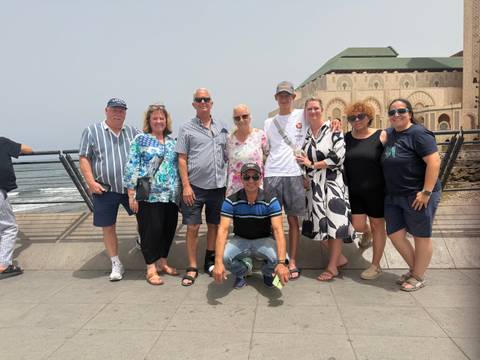       Tour group smiling in front of the grand Hassan II Mosque by the Atlantic ocean
  