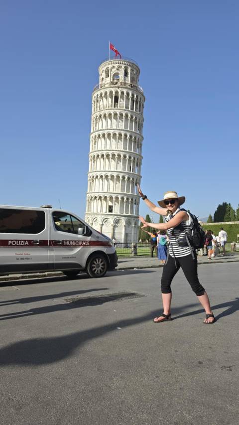       Tourist playfully posing as if supporting the Leaning Tower of Pisa with police van and visitors in the square
  