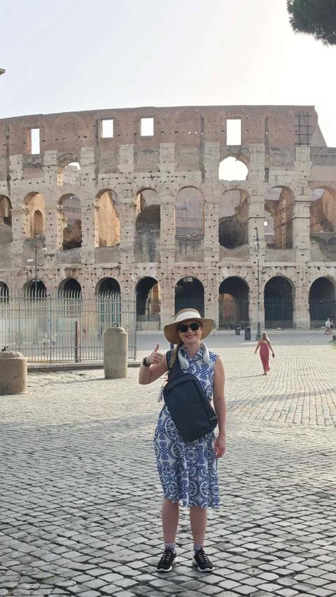       Female traveler giving a thumbs-up in front of the ancient arches of the Colosseum in Rome
  
