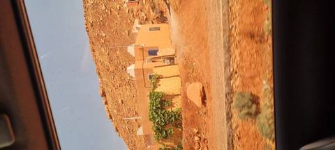       View from a car of a small desert house against a rocky hillside.
  