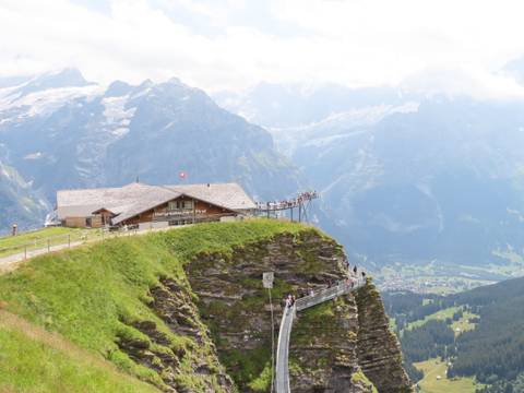       Clifftop restaurant and metal walkway overlook dramatic alpine valley and glaciers in Grindelwald.
  