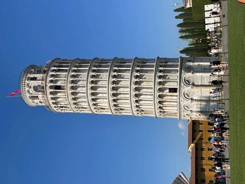       Leaning Tower of Pisa rises against clear blue sky with crowds of visitors at its base.
  