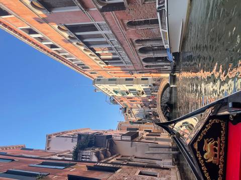       View from a gondola along Venice canal lined with pastel palazzi and arched bridges.
  