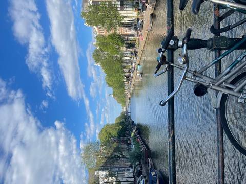       Classic Amsterdam canal scene with bike on bridge railings and boats along tree-lined waterway.
  