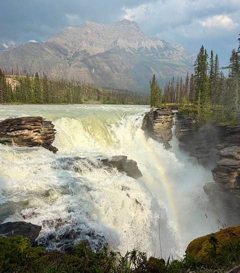       Powerful waterfall crashing through a rocky canyon with a visible rainbow in the mist.
  