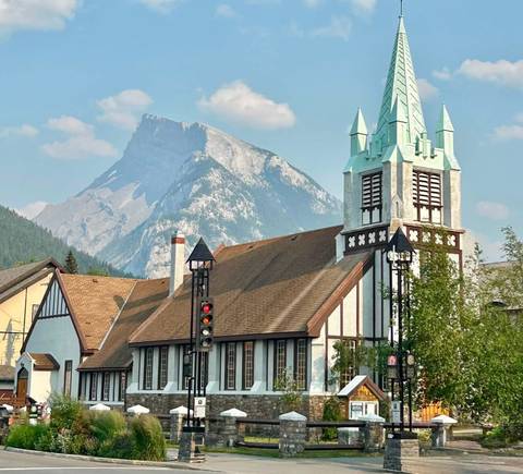       Alpine church with timber details set against a dramatic mountain backdrop in Banff town.
  