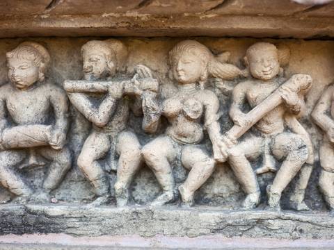       Weathered stone relief of musicians and dancers carved into the base of an ancient Indian temple.
  
