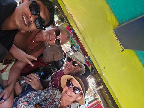       Casual selfie of four smiling travellers wearing sunglasses inside a brightly painted open vehicle.
  