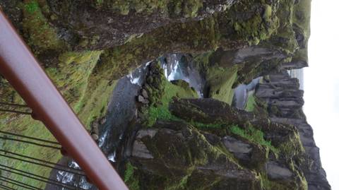       Vertical vista of moss-covered Fjadrargljufur canyon with river flowing far below.
  