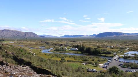       Expansive view over Thingvellir National Park rift valley with streams, church and parking area.
  