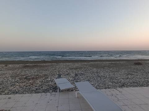       Quiet pebble beach with two empty loungers facing gentle evening waves and pastel sky
  