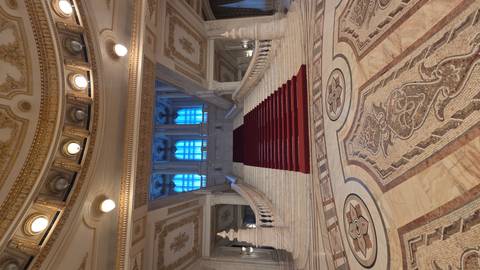       Grand marble staircase with red carpet and ornate ceilings inside the Palace of Parliament.
  