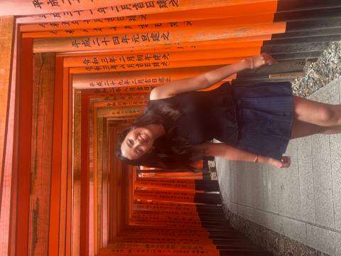       Woman walks through the vermilion corridor of torii gates at Fushimi Inari Shrine.
  