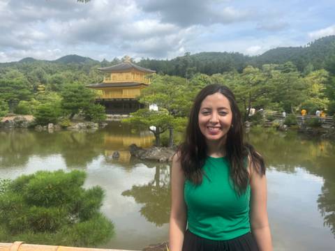       Visitor smiles in front of Kyoto's golden Kinkaku-ji pavilion reflecting in a tranquil pond.
  