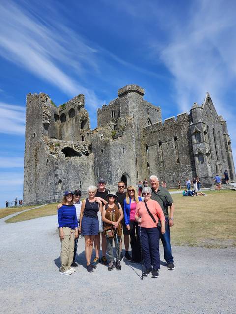       Group posing before the ancient stone walls and towers of the Rock of Cashel under a bright blue sky.
  