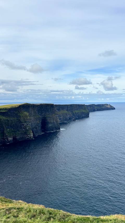       Sweeping panorama of the Cliffs of Moher stretching into the Atlantic under dramatic cloud cover.
  