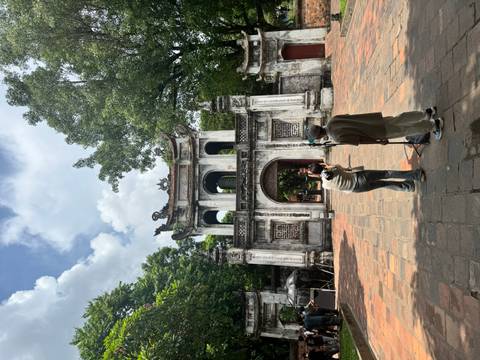       Visitors photograph each other in front of an ornate stone gateway inside a historic complex.
  