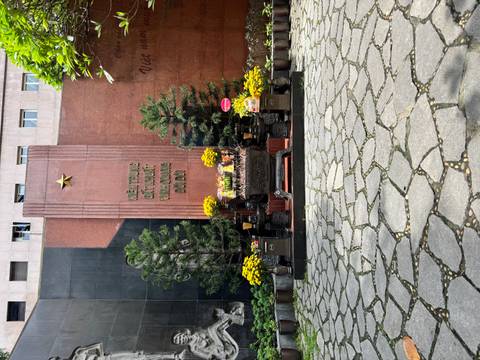       Outdoor memorial altar with yellow flowers and Vietnamese inscription set against stone walls.
  