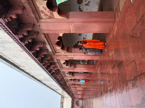       Visitors in colorful saris shelter under red-sandstone arches of a historical corridor on a rainy day
  