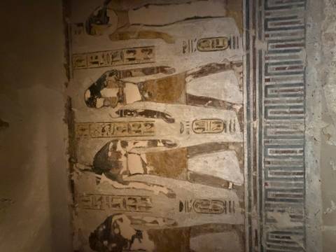       Faded wall painting depicting ancient figures with hieroglyphic inscriptions inside a tomb.
  