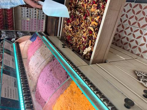       Colorful piles of ground spices line a glass display while a drawer overflows with dried fruit tea blends.
  
