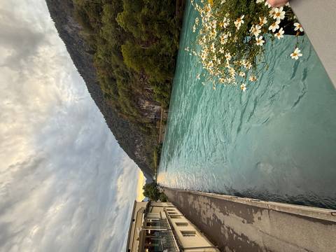       Turquoise river flowing between forested hills under cloudy sky.
  