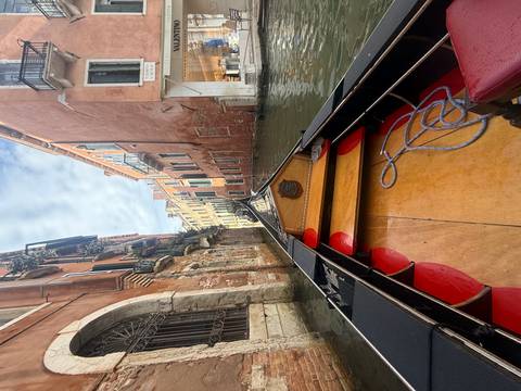       View from inside gondola along narrow Venetian waterway between tall houses.
  