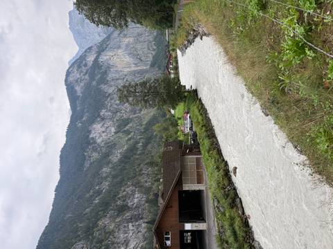       Rushing alpine river bordered by barns and steep forested mountainsides.
  