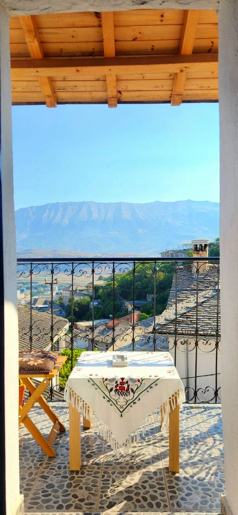       Mountain view framed by ornate balcony railing overlooking tiled rooftops of a stone-built town.
  