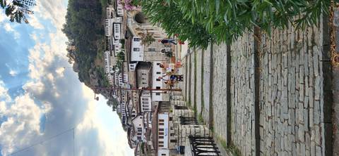       Cobblestone pathway leading through hillside village of white Ottoman-style houses with tourists strolling.
  
