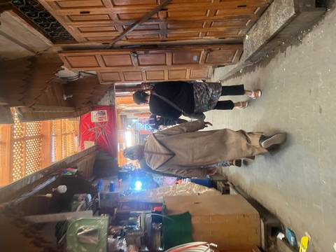       Narrow medina alley lined with wooden stalls as shoppers and robed locals walk through.
  