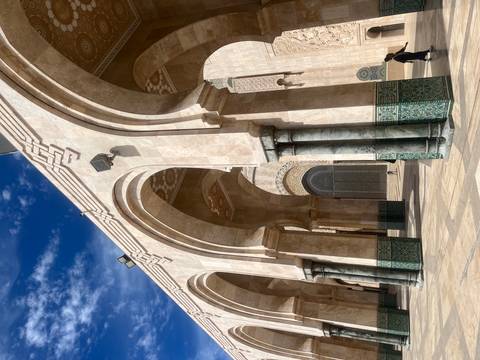       Series of elegant marble arches and columns of Hassan II Mosque courtyard against a blue sky.
  