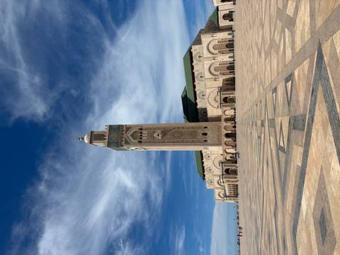       Wide view of the towering minaret and vast plaza of Hassan II Mosque under dramatic clouds.
  