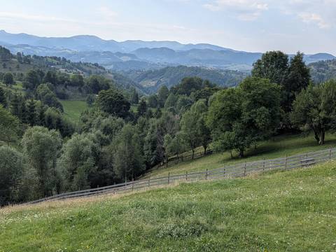       Serene mountain landscape with wooden fence lines, meadows, and hazy blue ranges in the background.
  