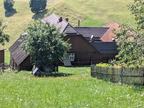       Traditional rural house with tin roof and surrounding garden fence beneath a sunny sky.
  