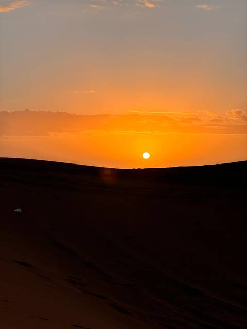       Brilliant orange sun setting over rolling sand dunes in the desert.
  