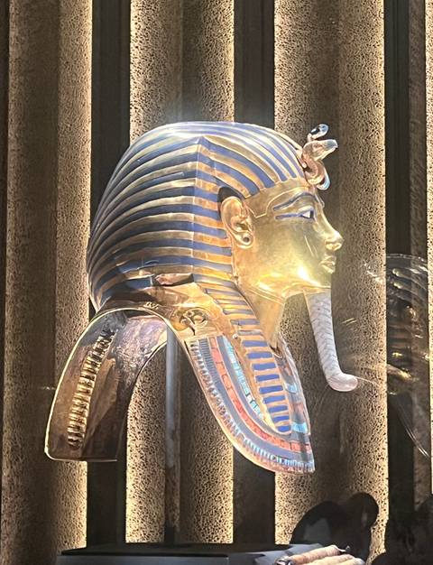       Close-up side profile of the gilded death mask of Tutankhamun displayed in a museum.
  